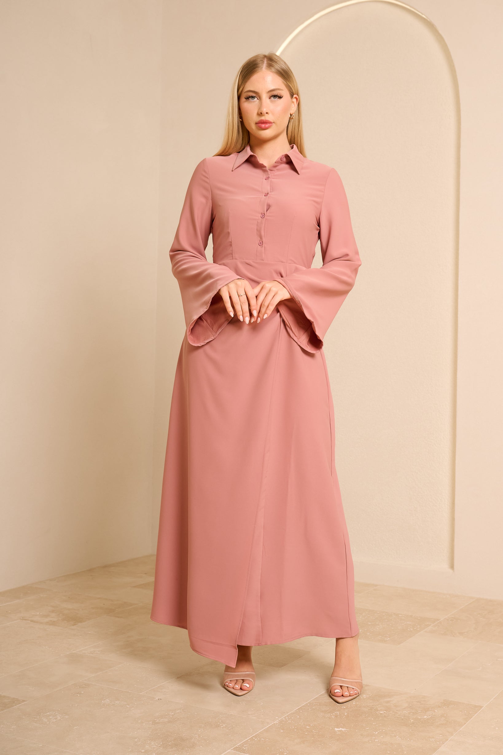 Woman wearing a pink dress standing against a beige background